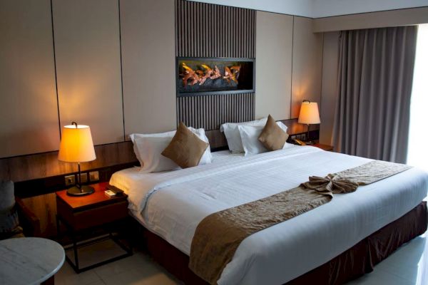 A cozy hotel room with a large bed, decorative pillows, bedside tables, lamps, and curtains. Soft lighting creates a warm ambiance.