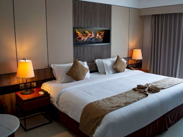 A cozy hotel room with a large bed, decorative pillows, bedside tables, lamps, and curtains. Soft lighting creates a warm ambiance.