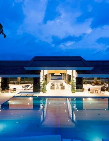 A luxurious, modern building with an illuminated pool in the foreground, set against a twilight sky.