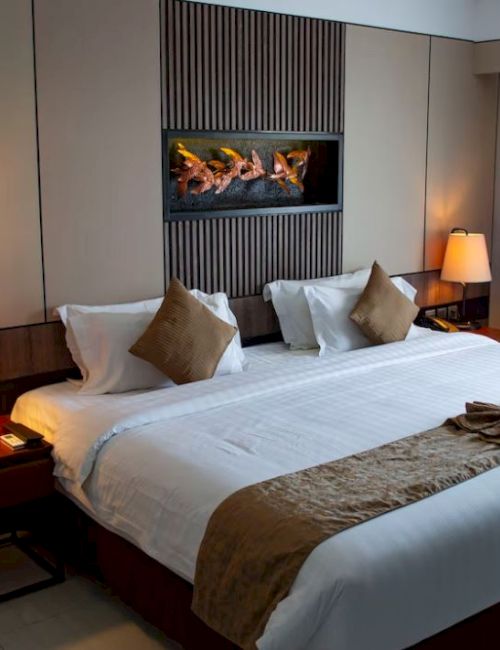 A modern hotel room with a neatly made king-size bed, two bedside tables with lamps, and a decorative piece above the bed's headboard.