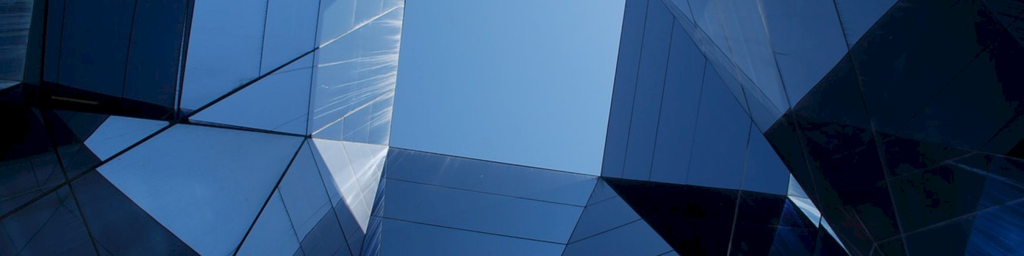 Geometric architectural design with reflective glass panels forming a symmetrical pattern, looking up towards a blue sky.