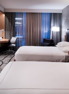 The image shows a modern hotel room with two neatly made beds, a desk with a chair, a wall-mounted TV, and stylish decor ending the sentence.