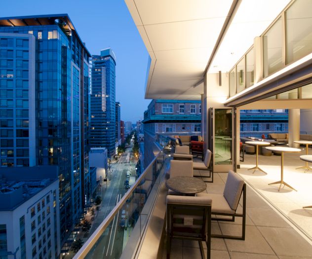 A modern terrace at twilight with seating areas and tables is overlooking an urban cityscape with tall glass buildings and illuminated streets.