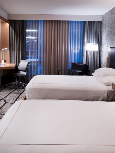 A modern hotel room with two beds, a flat-screen TV, a desk with a chair, and stylish decor.