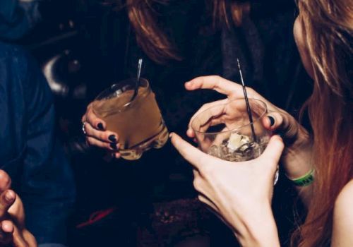 People are gathered, holding drinks and socializing in a lively setting, possibly a party or bar. They appear to be enjoying their time together.