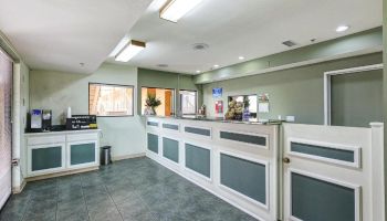 The image shows an empty reception area with a counter, a small waiting area, and a door. There are lights on the ceiling.