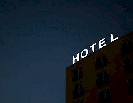 A building with a sign reading "HOTEL" is shown at night, with the letter "E" not illuminated.