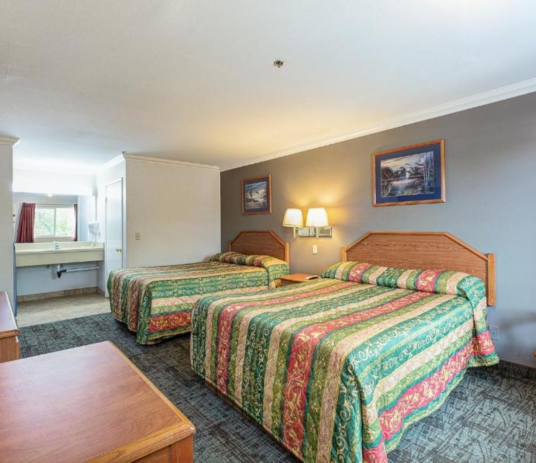 A hotel room with two beds, a desk, and a bathroom in the background.