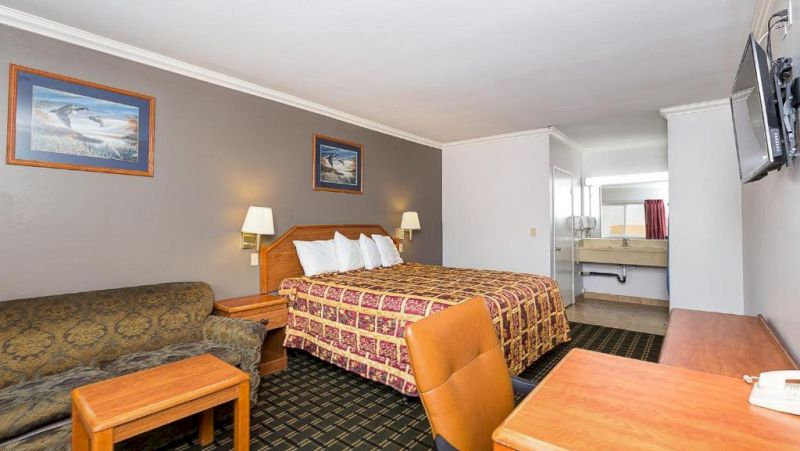 A wide view of a hotel room with a queen bed, sofa, desk, TV, and bathroom in the background.
