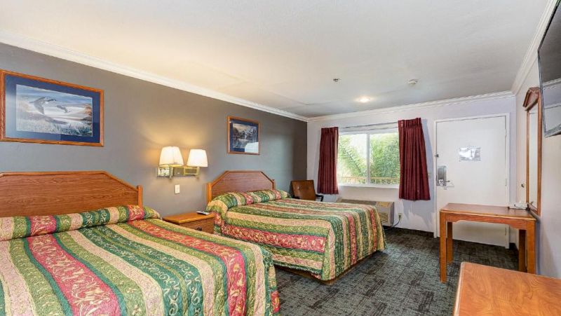 A hotel room with two beds, a desk, and a window.