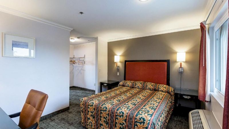 A hotel room with a bed, chair, nightstand, and window