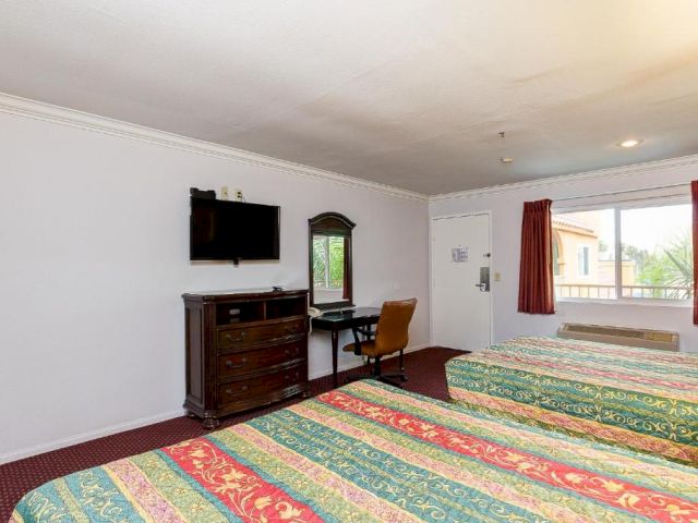 A hotel room with two beds, a dresser, TV, desk, and window.