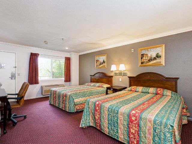 A hotel room with two beds, a desk, and a window.