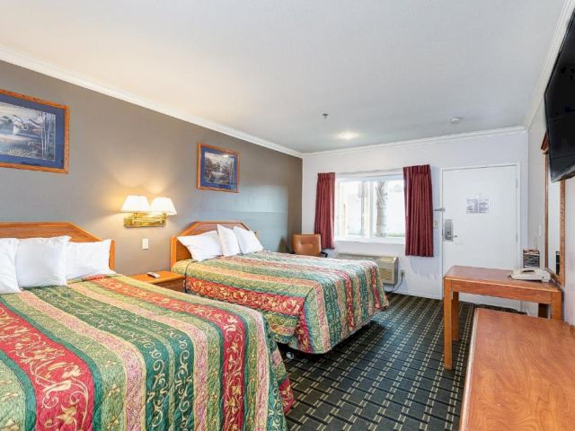 A hotel room with two beds, a desk, and a TV on the wall.
