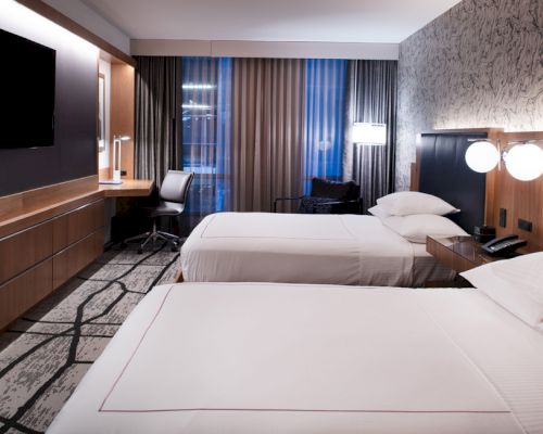 A hotel room with two beds, a desk, TV, and chair.