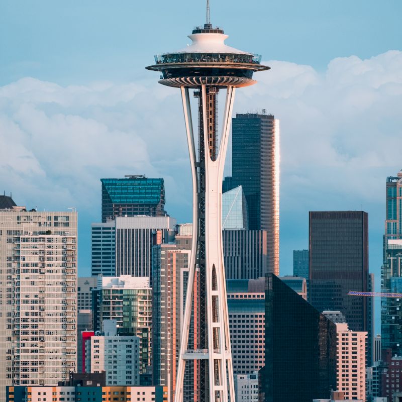 This image shows the Seattle skyline with the Space Needle prominently in the foreground, surrounded by various high-rise buildings on a clear day.