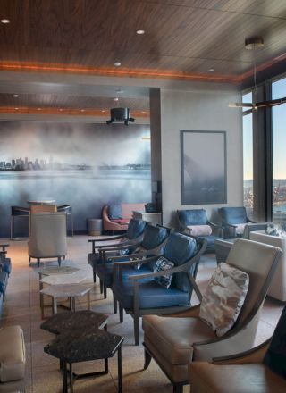 A modern, upscale lounge with plush seating, floor-to-ceiling windows showing a scenic waterfront view, and warm ambient lighting.