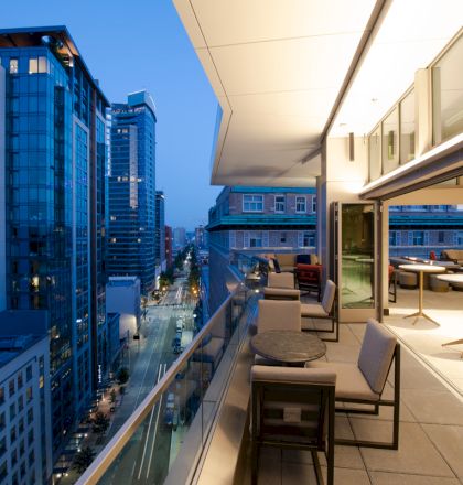 A modern rooftop terrace overlooking a cityscape with high-rise buildings; it features seating and tables with an indoor-outdoor flow.