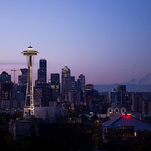 This image depicts the skyline of Seattle, Washington, with the iconic Space Needle and Mount Rainier in the background, during twilight.