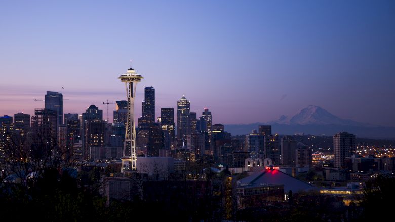 A cityscape of Seattle at twilight, featuring the Space Needle and various skyscrapers with Mount Rainier visible in the distance.