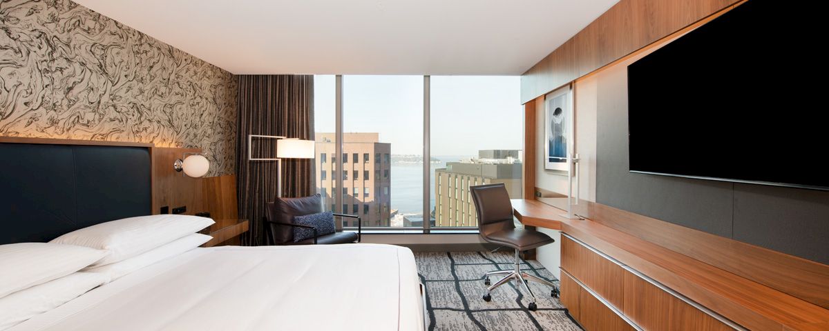 A hotel room with a bed, desk, chair, and TV in front of a window.